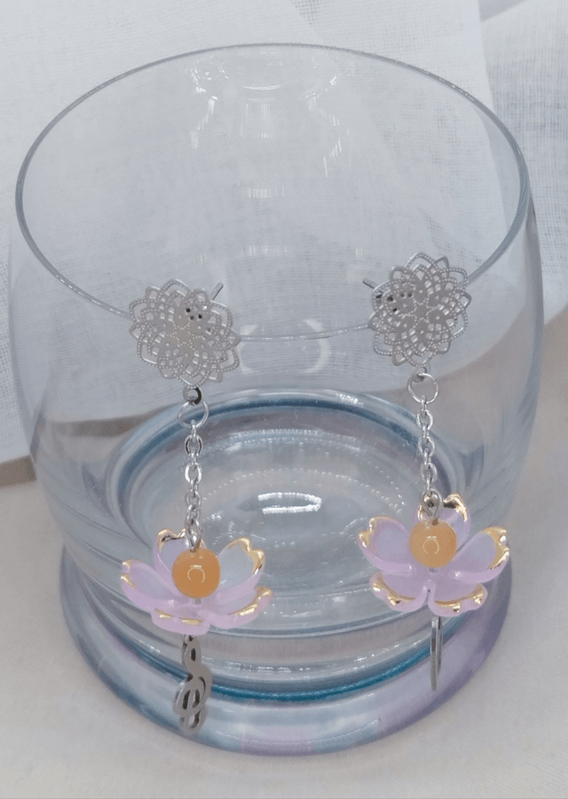 Clous d'oreilles fleur en acier inoxydable, ornés d'une fleur acrylique avec perle naturelle, et pendentifs "cœur" et "clé de sol" en acier.